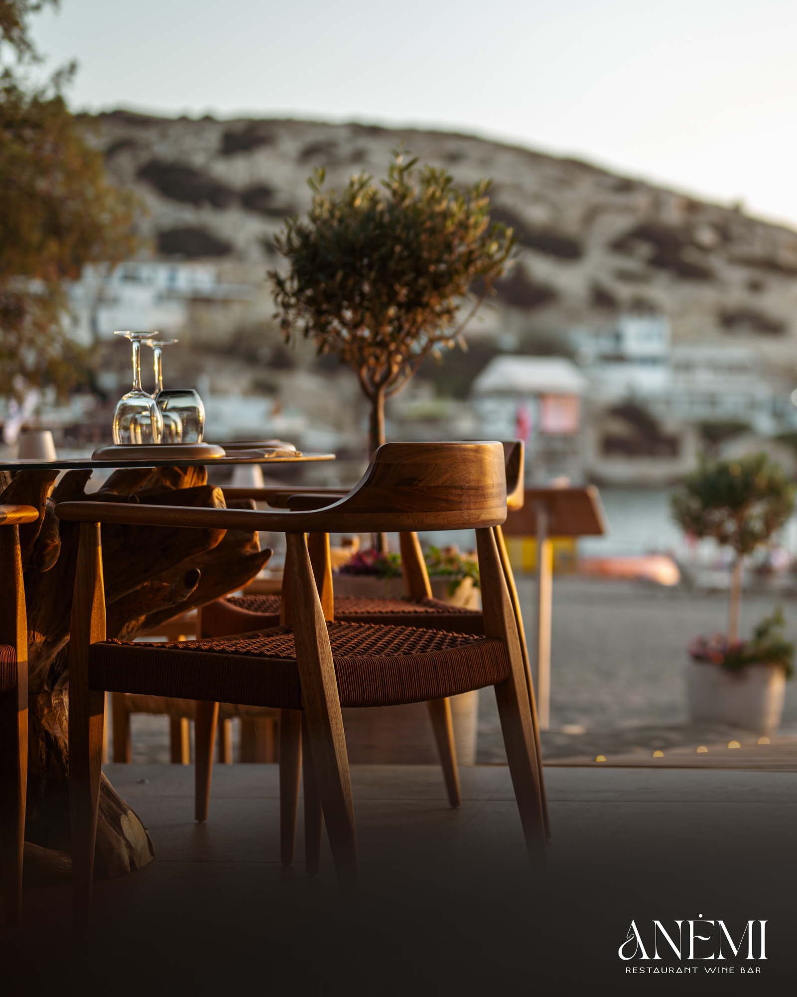 Table set with wine glasses overlooking Matala bay at golden hour